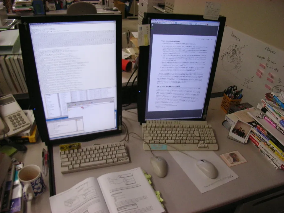 Escritorio de oficina con dos monitores, teclado y notas adhesivas amarillas pegadas en los marcos de las pantallas.