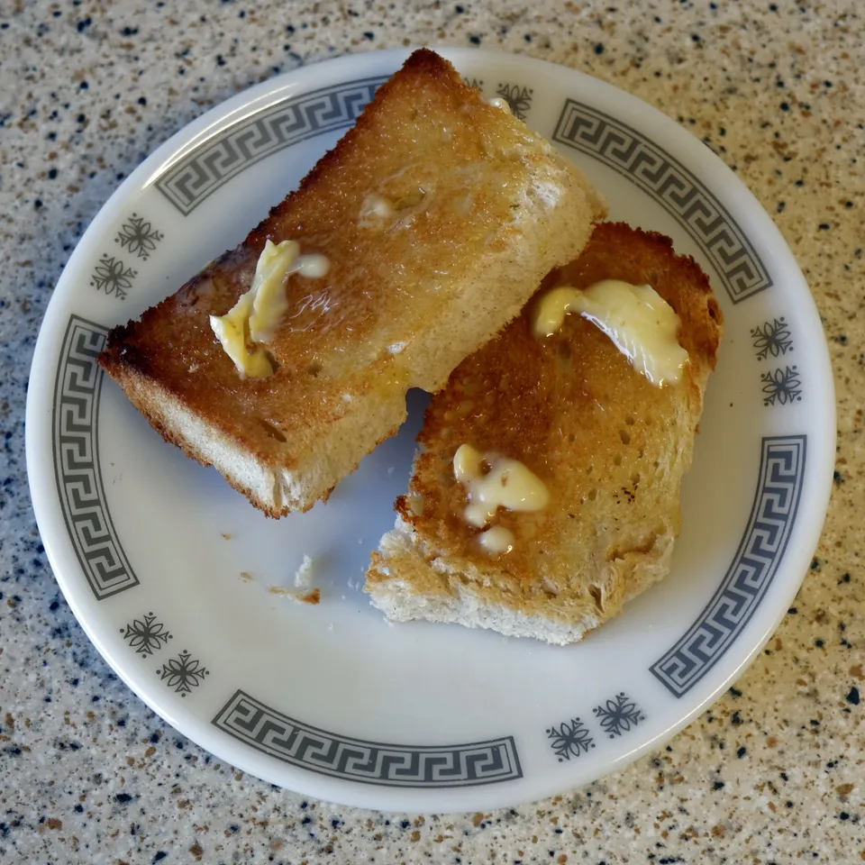 Dos rebanadas de tostada con mantequilla sobre un plato, vista desde arriba