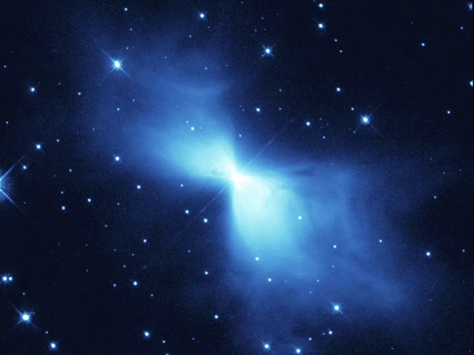 Nebulosa con forma de reloj de arena en tonos azulados y verdosos sobre un fondo negro salpicado de estrellas