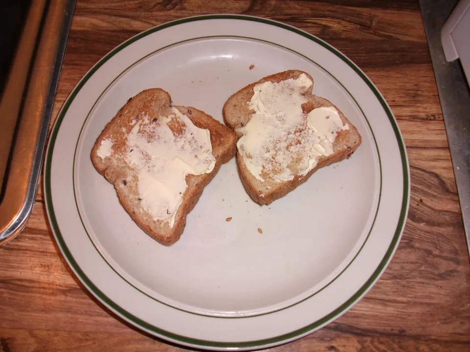 Dos rebanadas de pan tostado untadas con mantequilla sobre un plato blanco